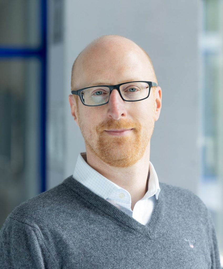 Man with glasses smiling softly.